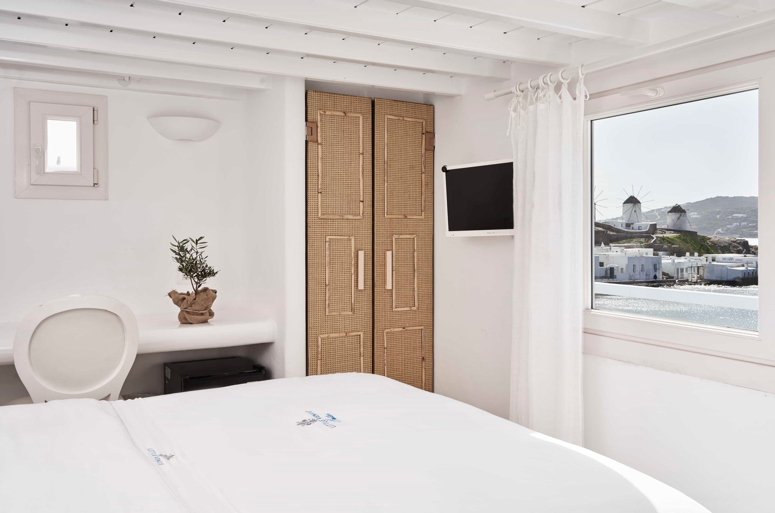 Bed facing a window that frames the Mykonos windmills