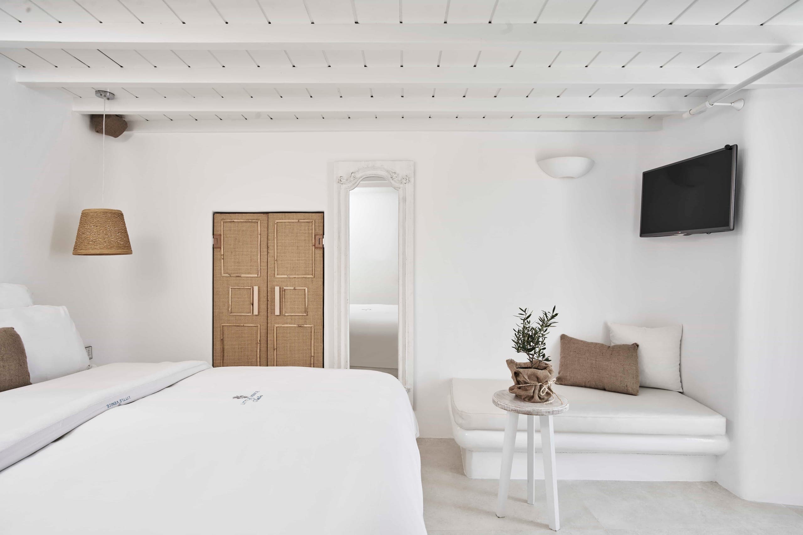 White Cycladic bedroom with queen bed, built-in sofa, wooden doors and wall-mounted TV