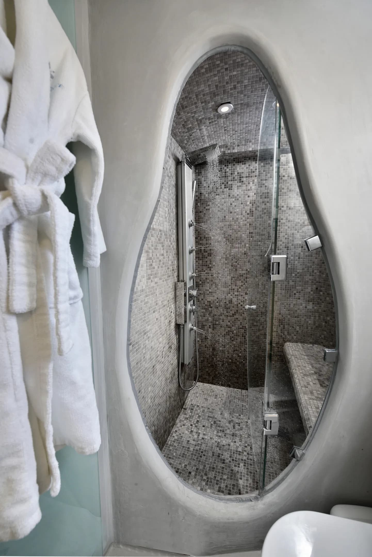 Steam shower behind a curved glass opening and bathrobes
